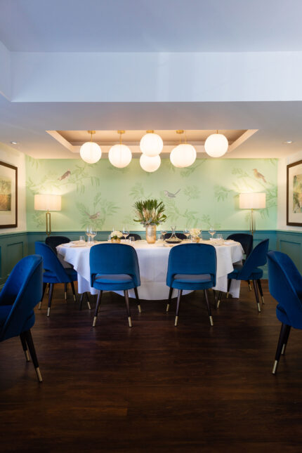 Private dining room featuring a large round table with a white tablecloth and blue velvet chairs for an exclusive funeral reception.
