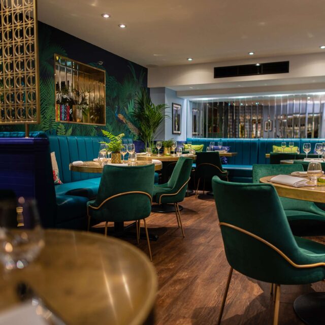 legant dining space featuring green velvet chairs, dark blue banquette seating, and set tables for a funeral reception.